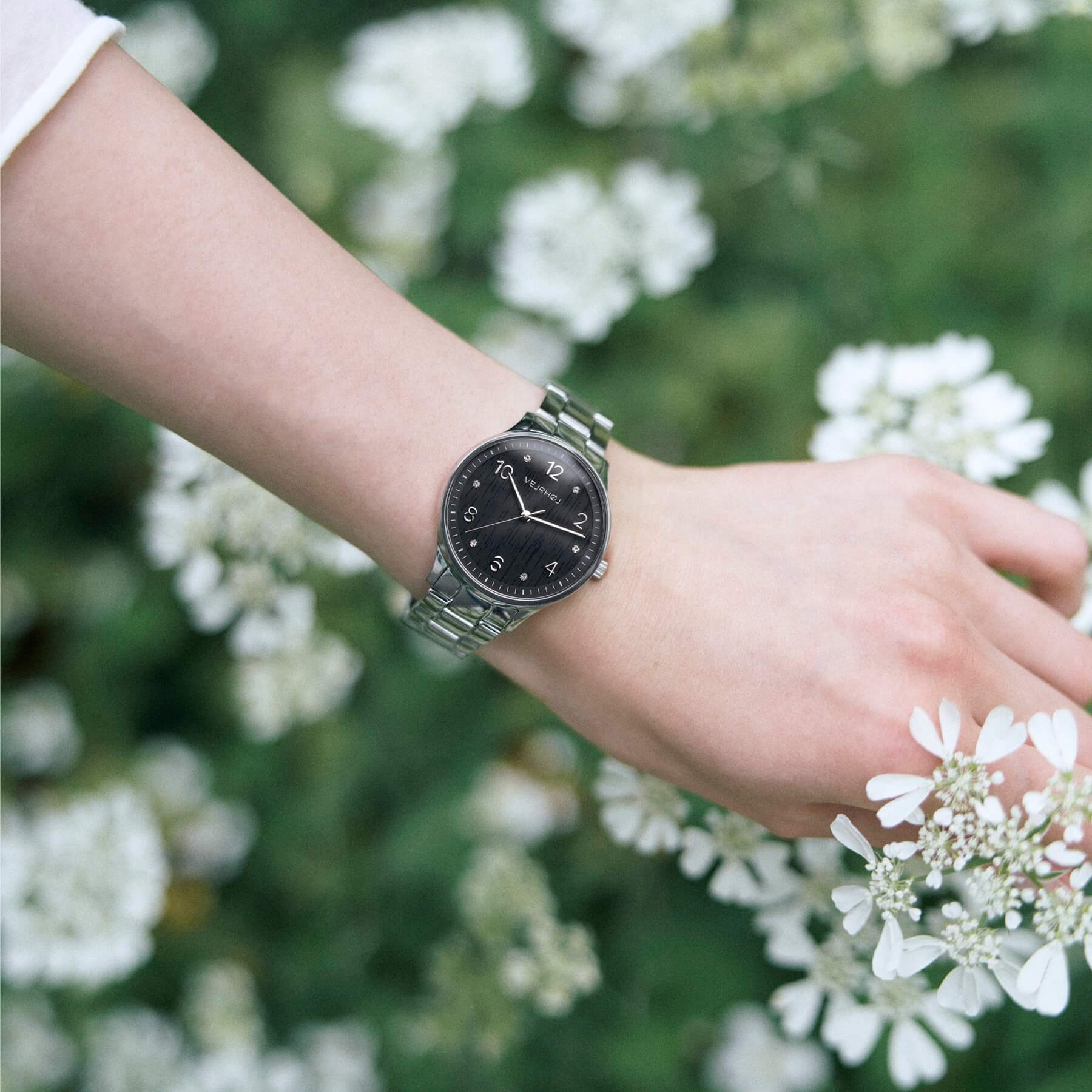 VEJRHØJのPetite Royal Black、自然光の中で草花に溶け込むように映える黒い木目フェイスのレディースウォッチ