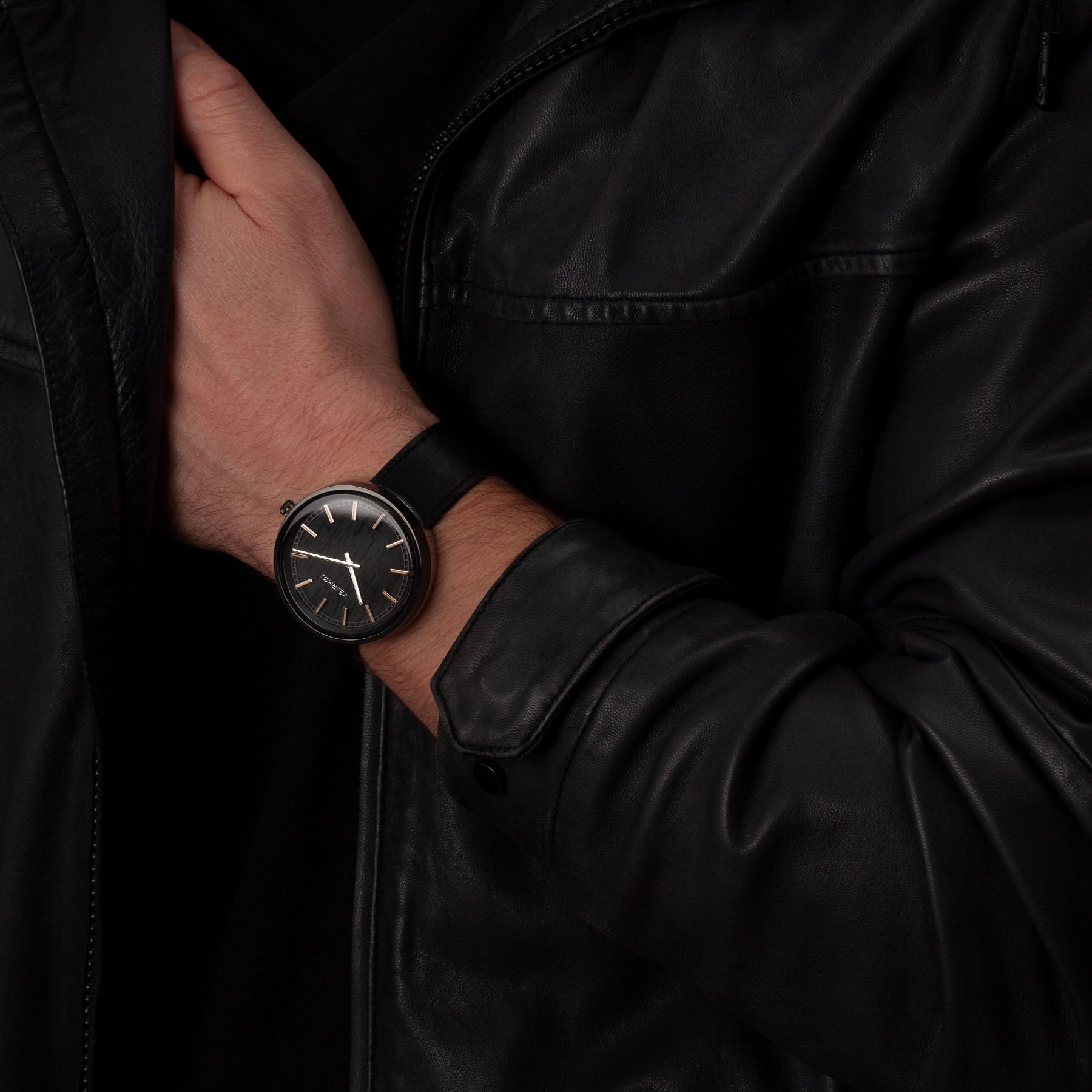 VEJRHØJの腕時計、NORDIC NOIR。黒いダイヤルとブラックレザーバンドが特徴のエレガントなデザインを、黒いジャケットを着た手首に装着している