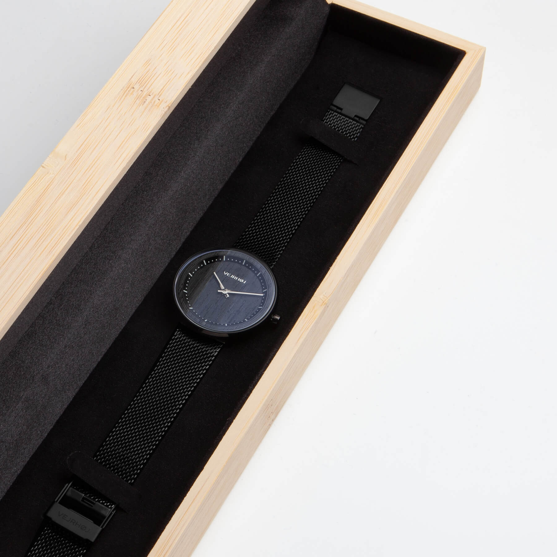 竹製の箱の中に置いてあるメッシュバンドのついた黒いレディース用の腕時計
