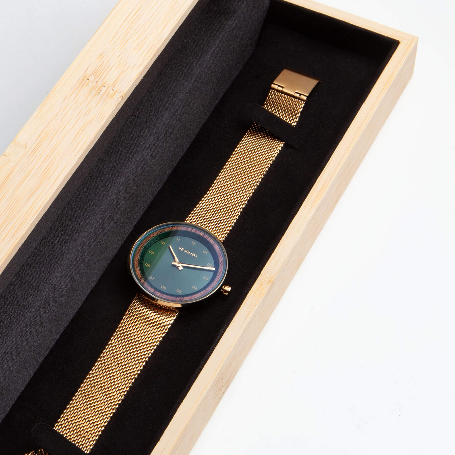 メッシュバンドのついた緑とゴールドの腕時計が竹箱の中にある