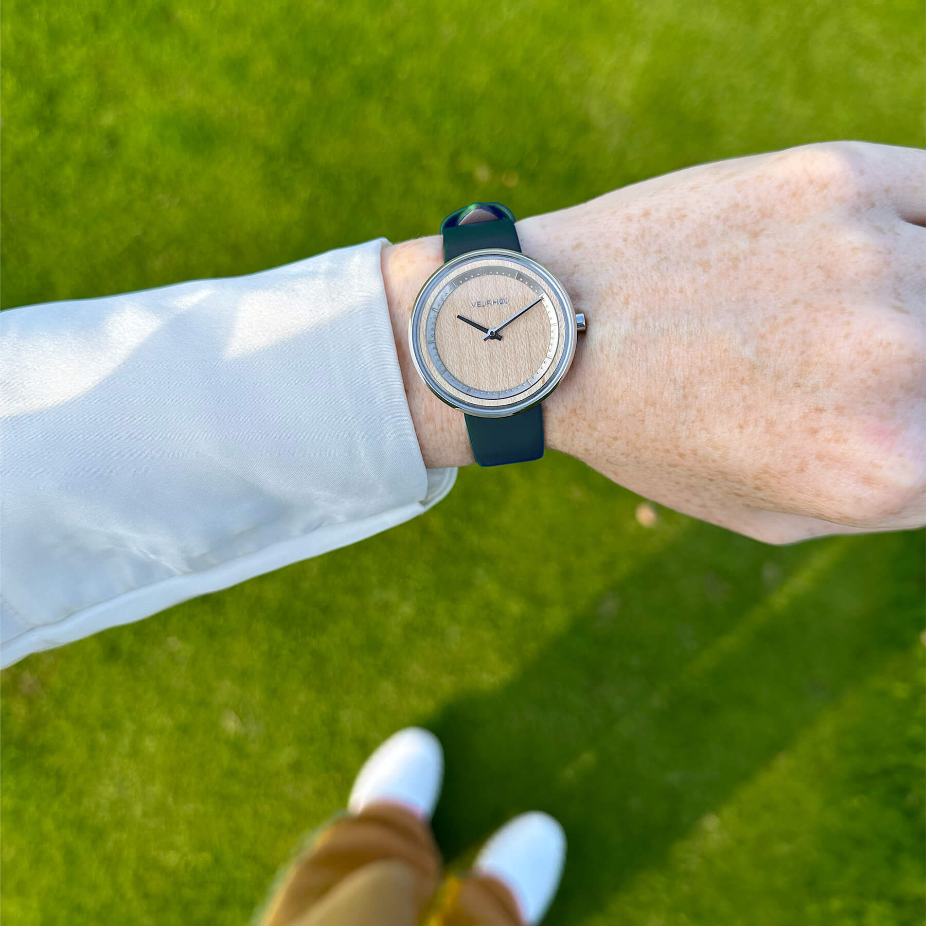 芝生の背景に、人の手首についたストラップの緑の腕時計