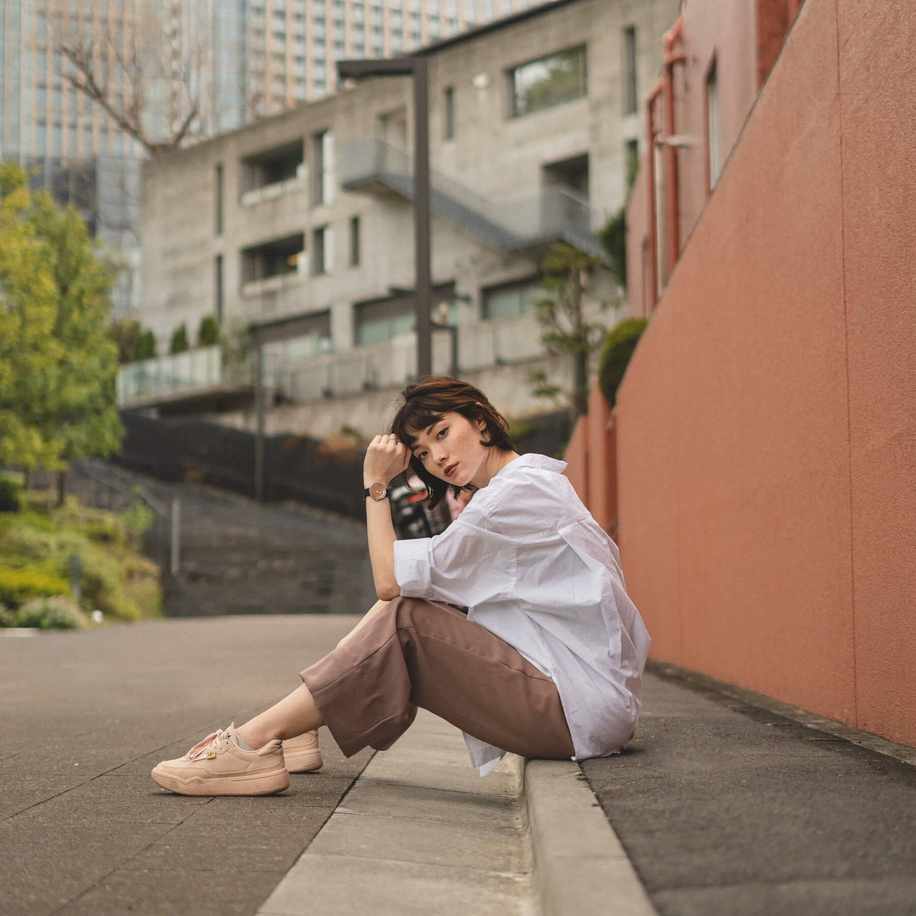 ヴェアホイの木製腕時計 Petite｜SAKURA を身に付け、道路に座っている白いシャツの女性