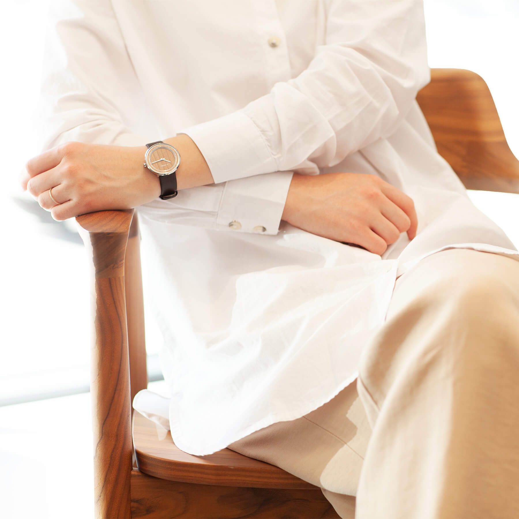 木製腕時計を身に付けた白いシャツの女性が木の椅子に座っている様子