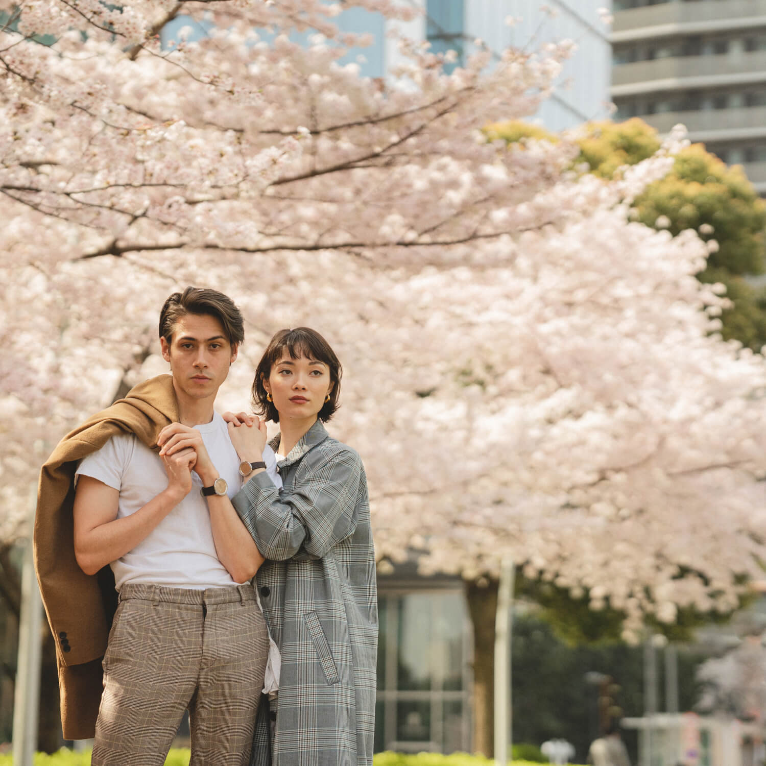 北欧ブランドVEJRHØJのペアウォッチを身につけた桜の木の前で肩を組むカップル